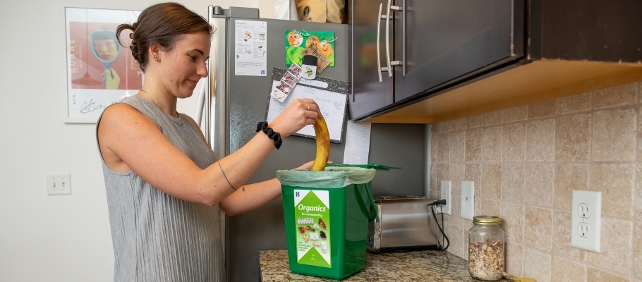 Woman putting banana peel in compost bin in kitchen