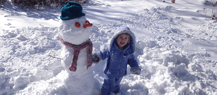 Young girl playing in the snow with a snowman